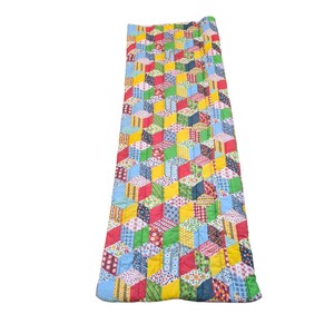 May include: A colorful, geometric quilt with a repeating pattern of 3D cubes. The quilt features a variety of fabrics in red, yellow, blue, green, and white. The quilt is rolled up at the top and appears to be a sleeping bag or mat.