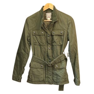 May include: An olive green utility jacket featuring a high collar, a front zipper closure with a snap-button placket, four front pockets with snap-button flaps, and a matching fabric belt with a metal buckle at the waist for a cinched fit.