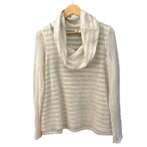 May include: A cream-colored, long-sleeved sweater with a cowl neck and horizontal stripes. The sweater is hanging on a wooden hanger against a white background. The fabric appears to be lightweight and slightly sheer.