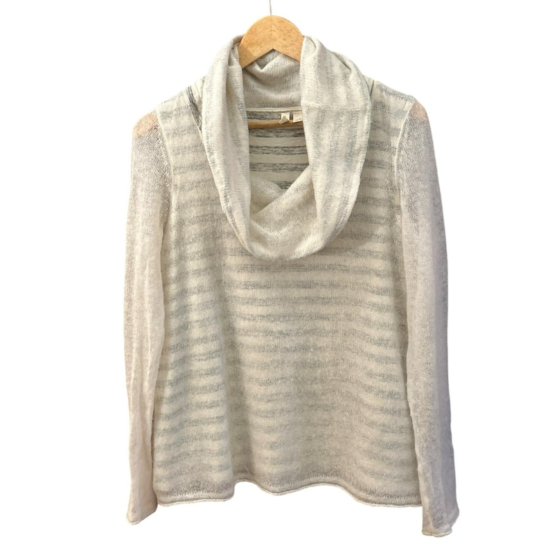 May include: A cream-colored, long-sleeved sweater with a cowl neck and horizontal stripes. The sweater is hanging on a wooden hanger against a white background. The fabric appears to be lightweight and slightly sheer.