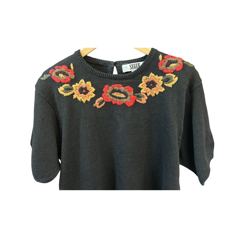 May include: Black short-sleeved sweater with embroidered floral design in red, yellow, and brown. The flowers are arranged across the shoulders and neckline. The label reads "SEGUE". The sweater is hanging on a wooden hanger.