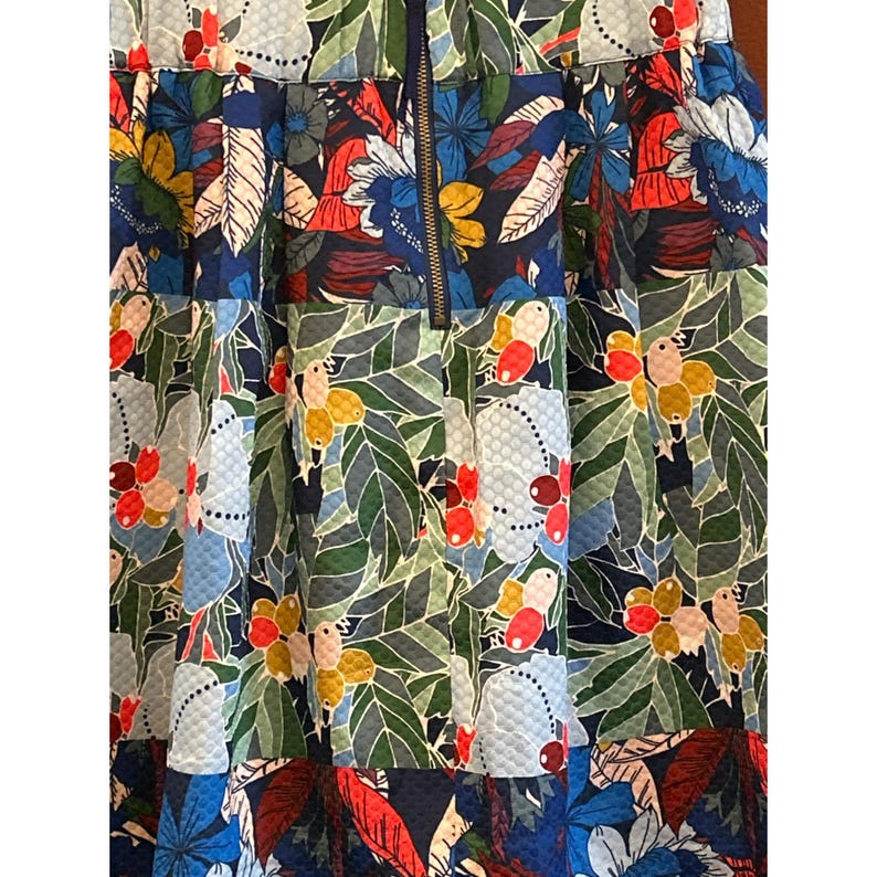 Puede incluir: Una falda de estampado floral azul, verde, rojo y blanco con cierre de cremallera. La falda tiene una tela texturizada y un dise&ntilde;o plisado.