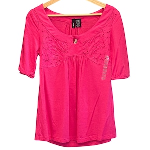 Könnte beinhalten: Ein leuchtend pinkfarbenes Oberteil mit kurzen Ärmeln, einem Rundhalsausschnitt und dekorativer Stickerei. Das Shirt hat einen Knopf und eine geraffte Taille. Ein Preisschild ist angebracht.