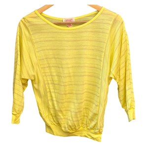 Könnte beinhalten: Ein leuchtend gelbes Langarmshirt mit Rundhalsausschnitt und einem dezenten horizontalen Streifenmuster. Das Kleidungsstück verfügt über einen gerippten Saum und Ärmelbündchen, wobei das Gitano-Markenetikett am Innenkragen sichtbar ist.