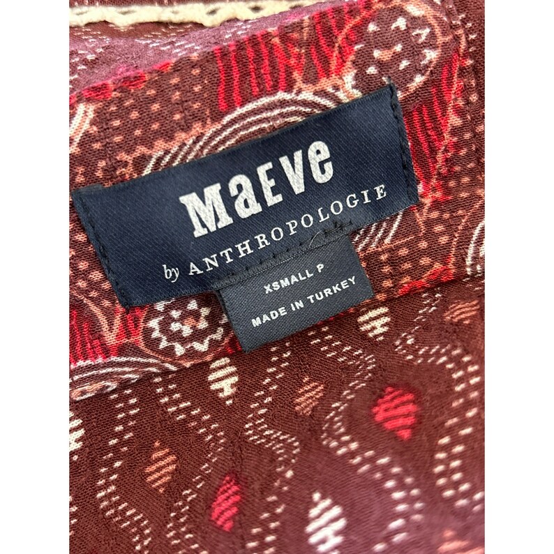 Puede incluir: Una etiqueta en blanco y negro con el texto "Maeve by Anthropologie" y "XSmall P Made in Turkey" sobre una tela estampada en rojo, blanco y marr&oacute;n.