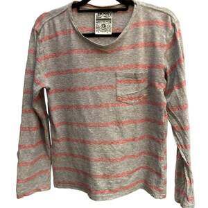 May include: Gray and red striped long-sleeve shirt with a small pocket on the left side. The shirt has a JUNKHEAD label with the text "AMERICAN MADE" on it.