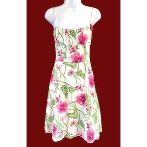 Puede incluir: Un vestido blanco de verano con estampado floral rosa y verde. El vestido tiene un corpiño ajustado y una falda fluida.