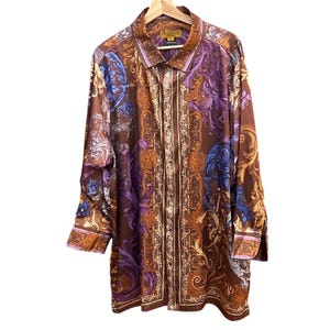 May include: A long-sleeved button-down shirt with a brown background and a baroque-style floral pattern in shades of purple, blue, orange, and gold. The shirt has a collared neckline and buttoned cuffs. The label reads "PRESTIGE".