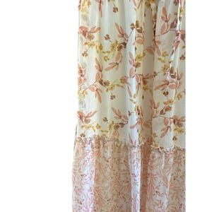 Pode incluir: Um vestido maxi branco com estampa floral em tons de rosa e amarelo. O vestido tem uma saia em camadas e um caimento solto e fluido.