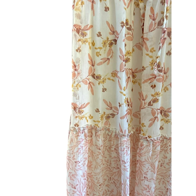 Pode incluir: Um vestido maxi branco com estampa floral em tons de rosa e amarelo. O vestido tem uma saia em camadas e um caimento solto e fluido.