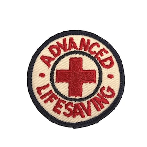 May include: Embroidered patch with the words "ADVANCED LIFESAVING" in red lettering around a red cross on a cream-colored background. The patch has a navy blue border.