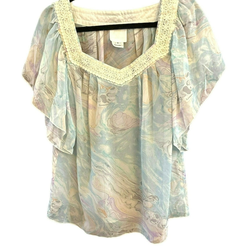 May include: A light blue sheer blouse with a white lace trim around the neckline. The blouse has a marbled pattern in shades of blue, pink, and white.