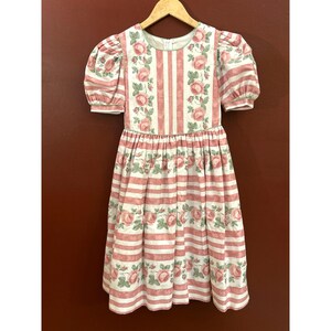 Puede incluir: Un vestido blanco y rosa con estampado floral y rayas rosas. El vestido tiene mangas abullonadas y una falda fruncida.