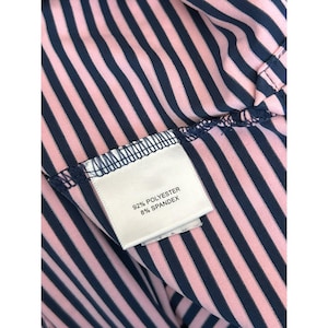 May include: Close-up of a pink and navy blue striped fabric. A white tag is sewn into the fabric, with the text "92% POLYESTER 8% SPANDEX". The fabric is folded, showing the texture and pattern of the material.