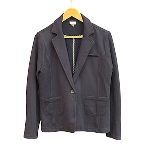 May include: A navy blue blazer with a single button closure, two front pockets, and a notched lapel. The blazer is hanging on a wooden hanger against a white background. The interior lining is visible.