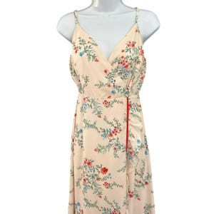 May include: A light pink maxi dress with a floral print featuring red, blue, and green flowers. The dress has a V-neckline, spaghetti straps, and a wrap-style bodice. The skirt has a ruffled hem.