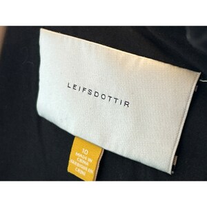 Op de afbeelding: Een wit label met de tekst "LEIFSDOTTIR" in zwarte letters. Een geel label met de tekst "10 MADE IN CHINA FABRIQUE EN CHINE" is bevestigd aan het witte label.