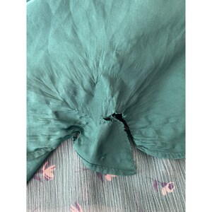 May include: A close-up of a teal green fabric with a small tear in the center. The fabric is wrinkled and has a silky texture.
