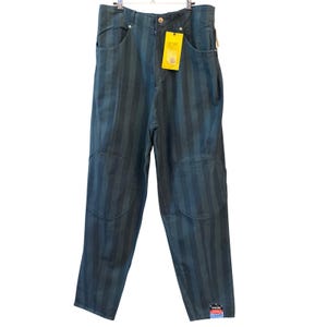 May include: High-waisted trousers in a dark teal and black vertical striped pattern. These pants feature reinforced circular knee patches, a front button closure, and a bright yellow rectangular tag attached to the waistband with visible text.