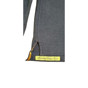 May include: A dark gray long-sleeve shirt with a yellow and orange trim on the side seam. The shirt has a yellow tag sewn on the bottom hem that reads "Knowledge Wisdom Truth".