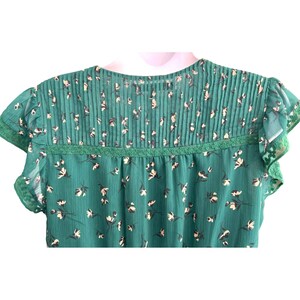 May include: A green floral print blouse with a ruffled neckline and short sleeves. The blouse has a lace trim around the neckline.