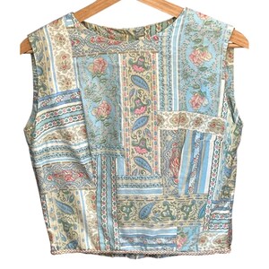 Può includere: Un top senza maniche caratterizzato da un design patchwork con vari pannelli di tessuto color azzurro, crema e verde salvia. Il motivo include disegni floreali, forme paisley e strisce verticali, rifinito con un bordo intrecciato sull'orlo.