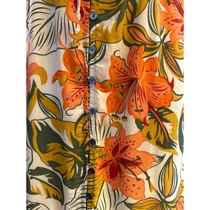 May include: A white button-up shirt with a floral print featuring orange, yellow, and green flowers. The shirt has a button-up closure and a collar.