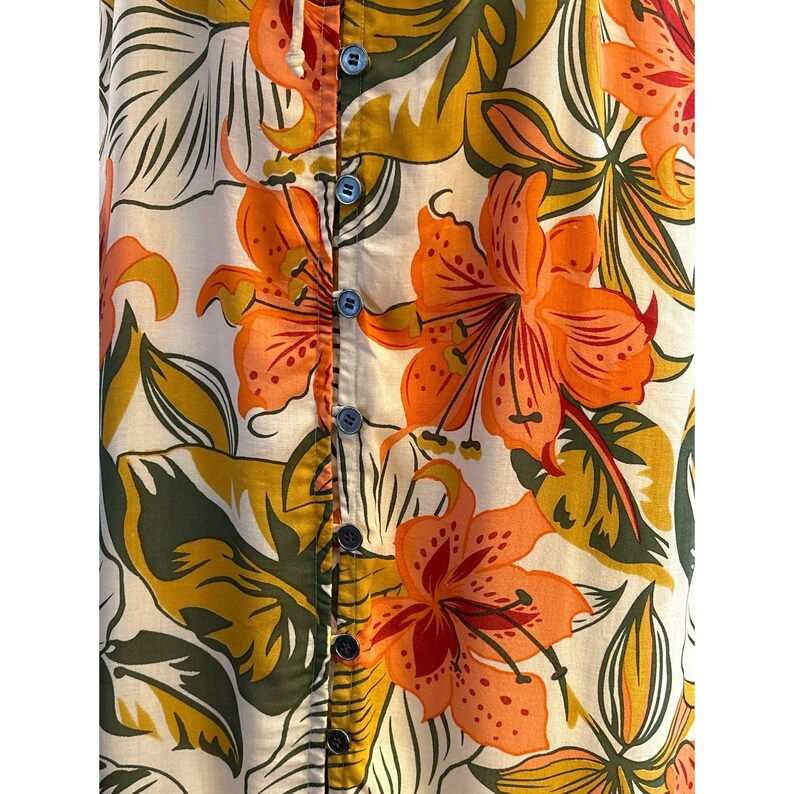 May include: A white button-up shirt with a floral print featuring orange, yellow, and green flowers. The shirt has a button-up closure and a collar.