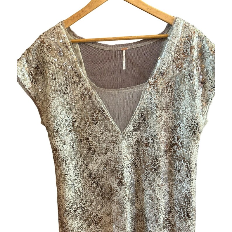 May include: A beige and silver sequined top with a V-neck and short sleeves. The top has a sheer, brown under layer.