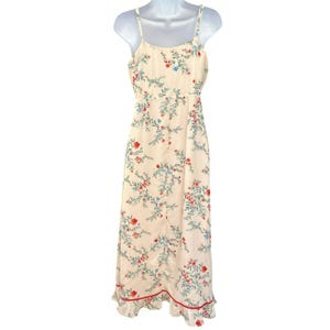 May include: A white maxi dress with a floral print featuring red, blue, and green flowers. The dress has thin straps and a ruffled hem.