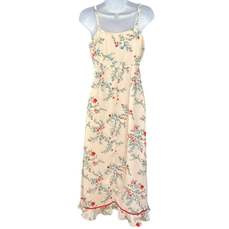 May include: A white maxi dress with a floral print featuring red, blue, and green flowers. The dress has thin straps and a ruffled hem.