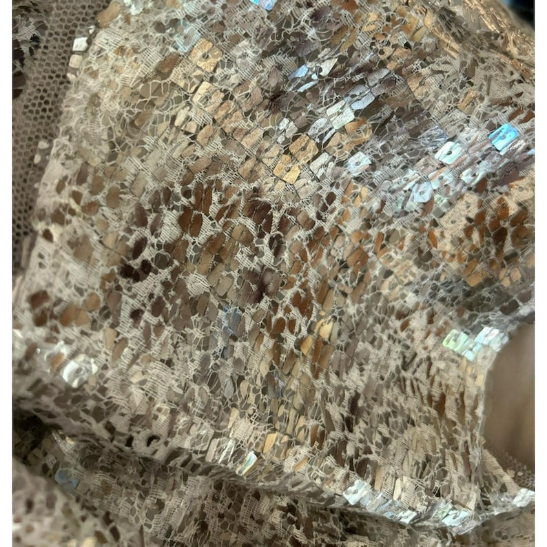 May include: Close-up of a beige fabric with a pattern of small, iridescent sequins. The sequins are arranged in a grid pattern and create a shimmering effect.