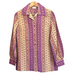 Blusa abotonada estilo años 70 de Sunny South, estilo retro bohemio, con estampado floral psicodélico en color morado y crema.