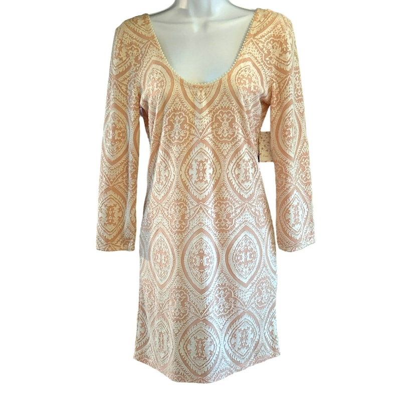 Puede incluir: Un vestido de color melocot&oacute;n con un patr&oacute;n geom&eacute;trico blanco. El vestido tiene un escote redondo y mangas tres cuartos.