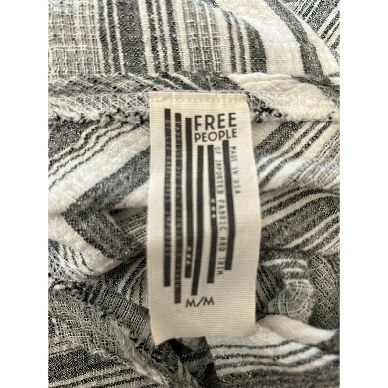 May include: A white and black striped fabric with a Free People tag attached. The tag is white with black text and a black and white striped design. The tag says "Free People" and "M/M".