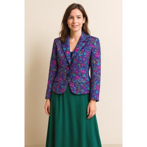Puede incluir: Una mujer con una blazer morada con estampado floral sobre un vestido verde. La blazer tiene una base azul oscuro con diseños florales rosas y turquesas. El vestido es de color verde oscuro liso.