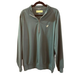 May include: A dark green long-sleeved pullover with a quarter zip closure. The pullover has a small embroidered logo on the left chest that says "Donald Ross" and features a small green leaf design.