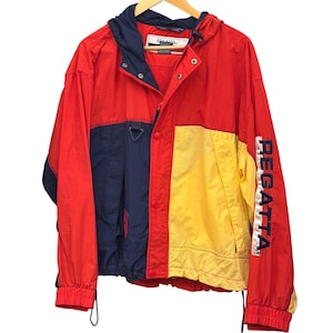 May include: A colour-blocked windbreaker jacket featuring red, navy blue, and yellow panels. The jacket includes a hood, a front zip closure with snap buttons, and the word REGATTA printed vertically in navy blue on the left sleeve.