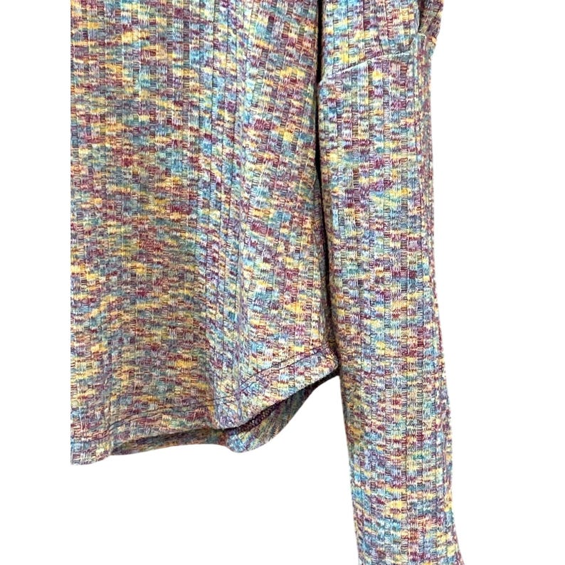 May include: A long-sleeved shirt with a colorful, abstract pattern in shades of blue, yellow, red, and purple. The shirt has a ribbed texture and a slightly cropped hem.