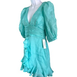 May include: A turquoise blue mini dress with a ruffled hem and a V-neckline. The dress has puffed sleeves and a fitted bodice. The dress has a tag that says "Bardot".