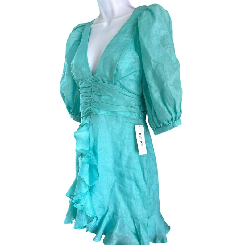 May include: A turquoise blue mini dress with a ruffled hem and a V-neckline. The dress has puffed sleeves and a fitted bodice. The dress has a tag that says "Bardot".