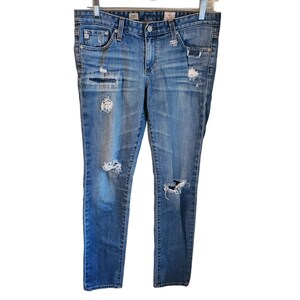 May include: Distressed blue denim jeans with multiple rips and tears throughout the legs. The jeans have a slim fit and a straight leg.