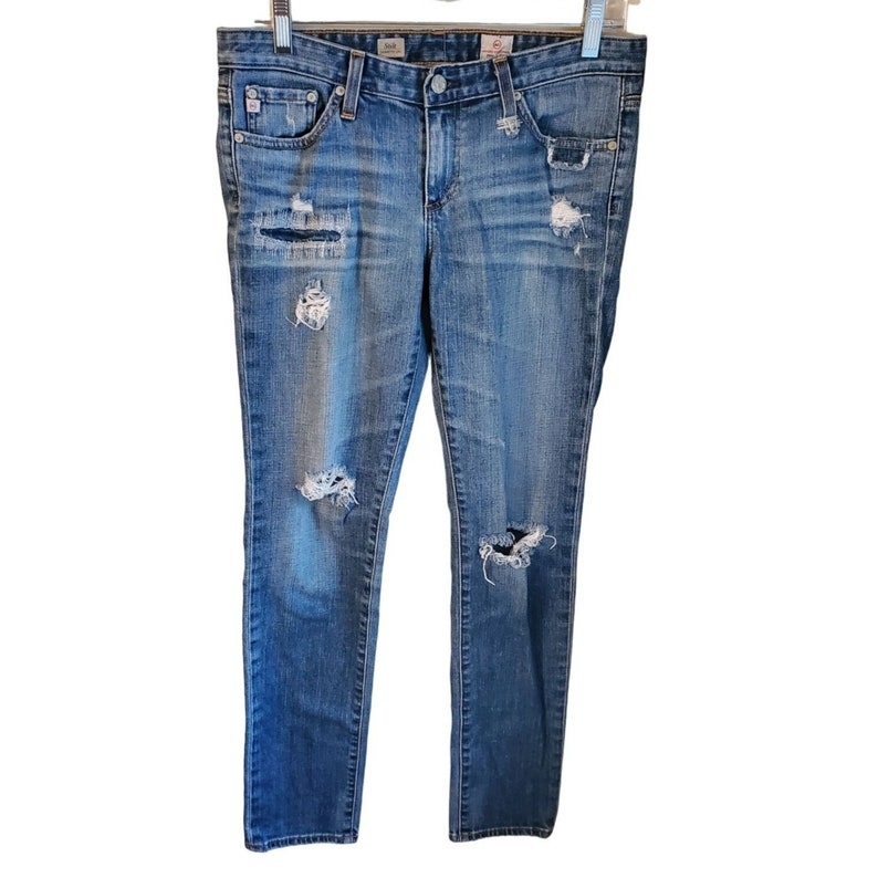 May include: Distressed blue denim jeans with multiple rips and tears throughout the legs. The jeans have a slim fit and a straight leg.