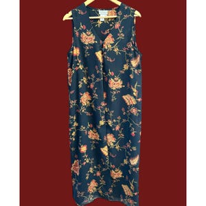 May include: A sleeveless, knee-length dress with a V-neck and a floral pattern. The dress is navy blue with a repeating pattern of orange, yellow, and pink flowers and leaves. The dress is hanging on a wooden hanger.