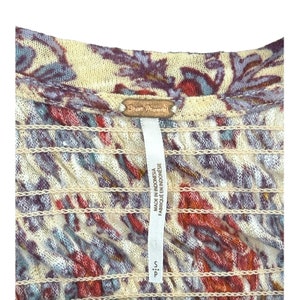 Peut inclure: Gros plan sur une chemise &agrave; motif floral beige, bleu et rouge avec une &eacute;tiquette Free People. L'&eacute;tiquette indique "Free People" et "Made in Indonesia, Fabrique en Indonesie". La chemise a une &eacute;tiquette de taille indiquant "S".