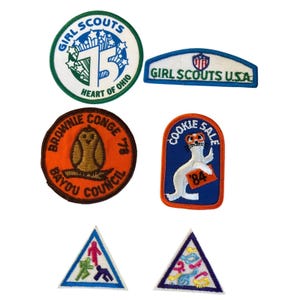 Peut inclure: Un ensemble de six écussons brodés comprenant un écusson rond du 75e anniversaire des Girl Scouts, un écusson rectangulaire Girl Scouts U.S.A., un écusson rond Brownie Council avec un hibou, un écusson Cookie Sale avec un phoque et deux écussons triangulaires.