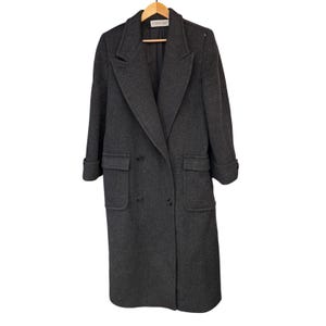 May include: A charcoal gray double-breasted wool-blend coat featuring a notched lapel, long sleeves with cuffed hems, and two large front flap pockets. The garment includes a Calvin Klein brand label at the inner neckline and black buttons.