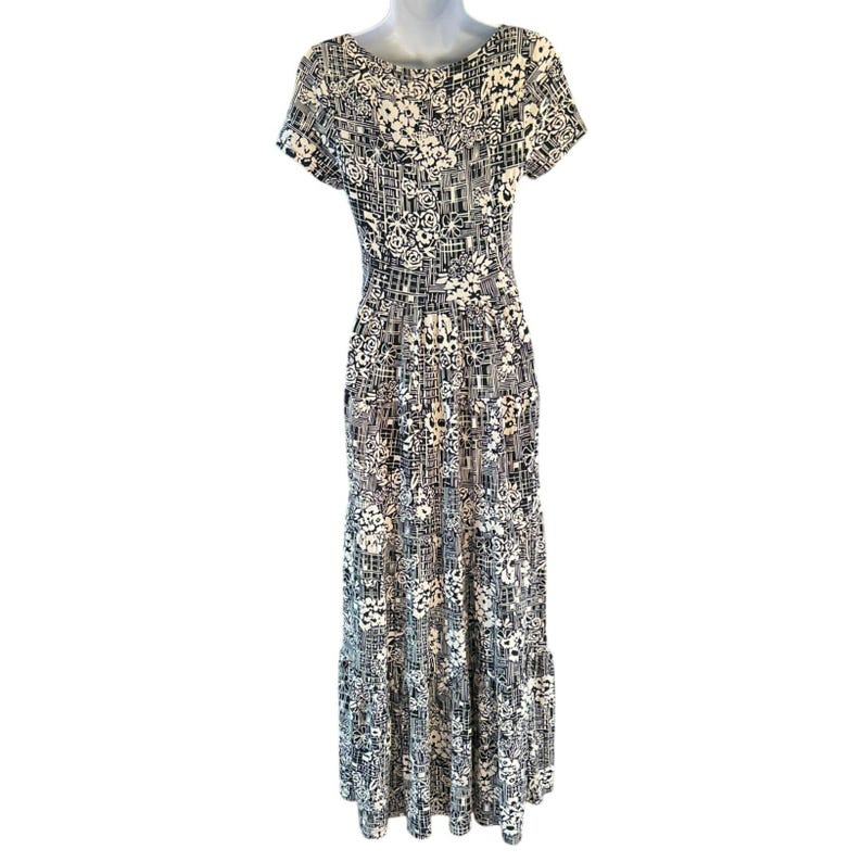 May include: A floor-length dress with a black and white floral and geometric pattern. The dress has short sleeves and a scoop neckline. The skirt has a tiered design. The dress is displayed on a mannequin.