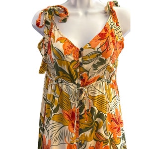 May include: A white, orange, and green floral print maxi dress with a button-up front and tie straps. The dress has a fitted bodice and a flowy skirt.