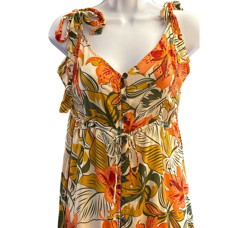 May include: A white, orange, and green floral print maxi dress with a button-up front and tie straps. The dress has a fitted bodice and a flowy skirt.